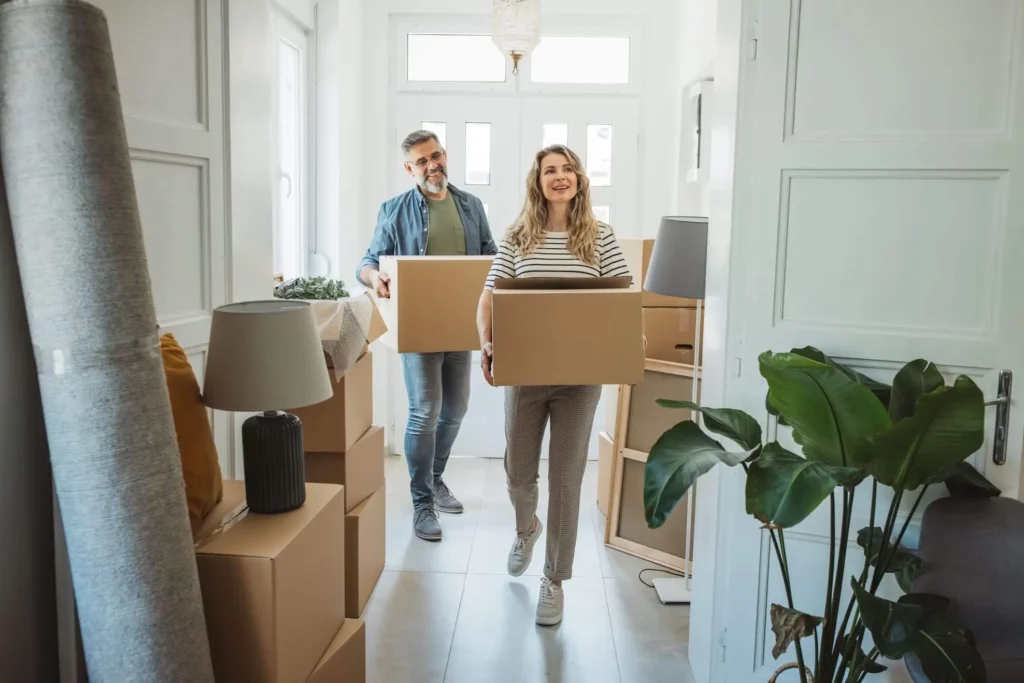 Imagem de um casal de homem e mulher entrando em um cômodo segurando caixas de mudança para ilustrar matéria sobre quais os cuidados ao alugar um imóvel