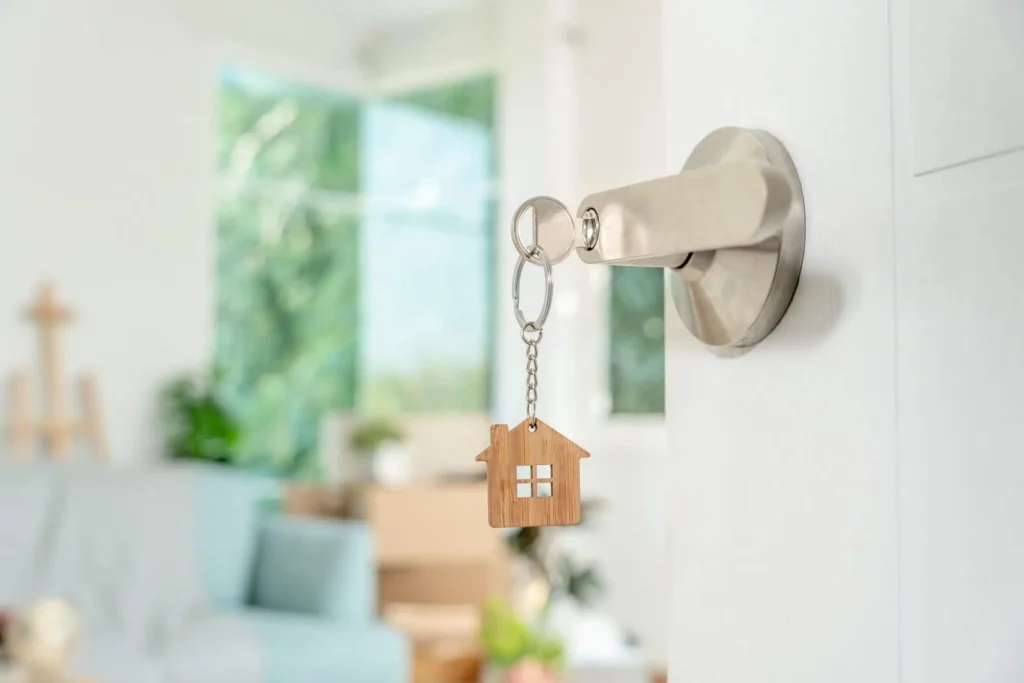 Imagem de uma chave com um chaveiro em formato de casa inserida na fechadura de uma porta aberta mostrando caixas e sofá de uma casa para ilustrar matéria sobre quando o proprietário pode entrar no imóvel alugado