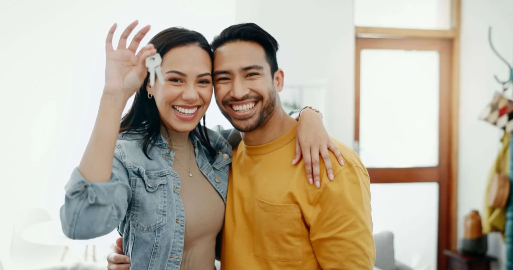 Imagem de um casal feliz se abraçando e segurando a chave de um imóvel para ilustrar matéria sobre se pode trocar a fechadura de casa alugada