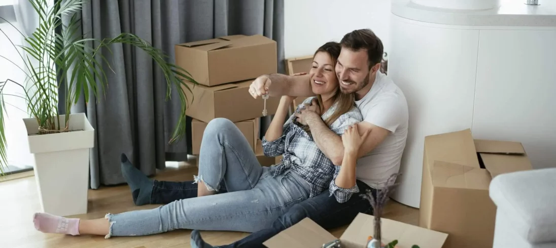 Imagem de um casal composto por um homem e uma mulher sentados no chão de uma casa ao lado de caixas de papelão para ilustrar matéria sobre o subsídio do Minha Casa, Minha Vida