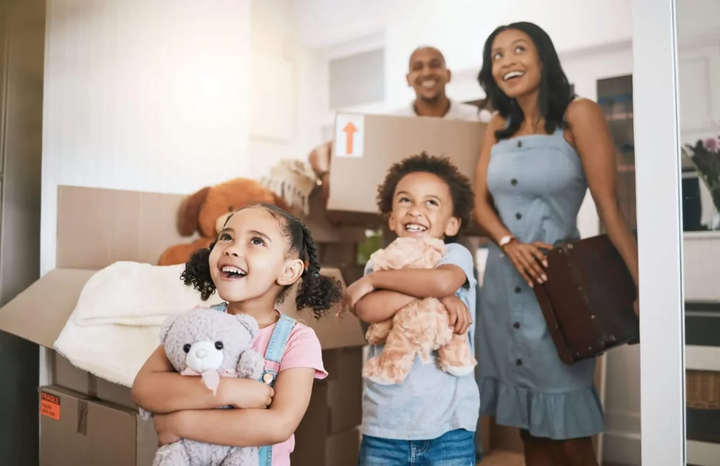 Imagem de uma família composta por um homem, uma mulher e duas crianças entrando em um imóvel com algumas caixas de papelão para ilustrar matéria sobre o subsídio do Minha Casa, Minha Vida